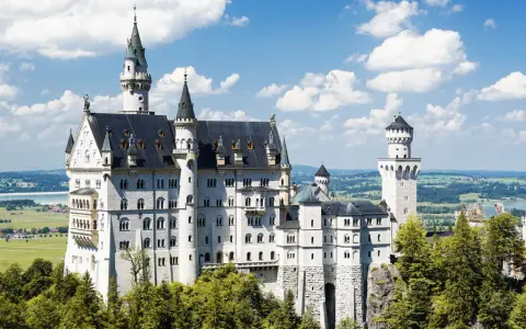 Schloss Neuschwanstein, ein Märchenschloss, dessen Geschichte von König Ludwig II. geprägt ist, thront majestätisch über grünen Hügeln und einem See.