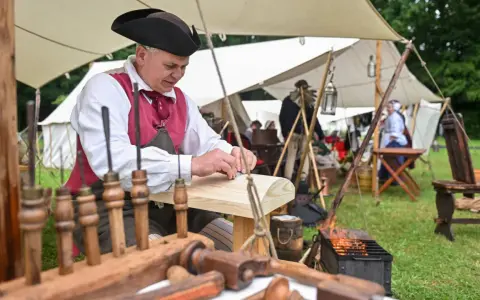 Ein Handwerker in historischer Kleidung arbeitet an Holz. Dies ist ein Beispiel dafür, was ist ein Freilichtmuseum: lebendige Geschichte zum Anfassen.