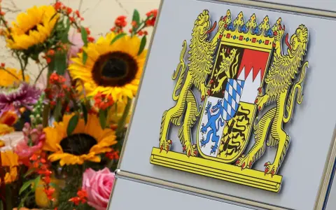 Das Staatswappen Bayerns, flankiert von Löwen, steht stolz neben einem bunten Blumenstrauß mit Sonnenblumen und Rosen.