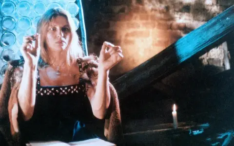 Annamirl Bierbichler in dunklem Kleid mit Pelzmantel, die Hände erhoben, im Schein einer Kerze.