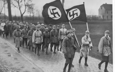 Männer marschieren mit Hakenkreuzfahnen. Ein historisches Bild, das an den Putschversuch Hitlers erinnert.