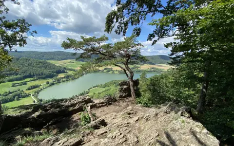 Felsiger Aussichtspunkt mit Kiefer über einem grünen Fluss und Hügeln in der Region Franken.