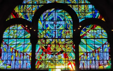 Farbenfrohe Glasmalerei eines Kirchenfensters mit biblischen Szenen und Engeln, die im Licht erstrahlen.