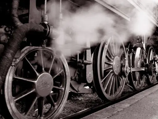 Dampf steigt auf von den Rädern einer historischen Lokomotive, ein Symbol für die Erfindung der Eisenbahn und den Beginn einer neuen Ära.