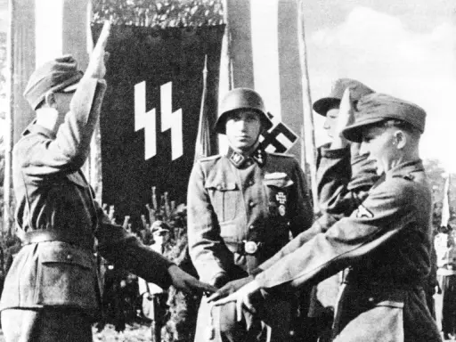 Mehrere SS-Soldaten stehen vor einer Fahne mit SS-Runen. Einer hebt den Arm zum Gruß.