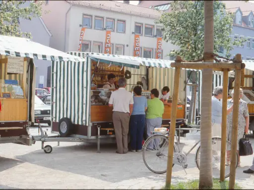 Marktstände in Neukirchen Balbini mit Brot und Butter. Menschen kaufen ein, ein Fahrrad steht bereit.