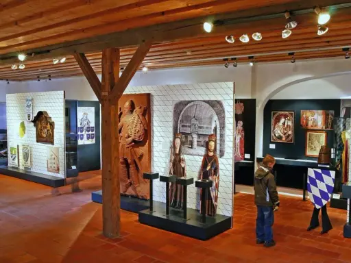 Museumsausstellung mit historischen Artefakten, darunter das Wittelsbacher Wappen, Skulpturen und Gemälde.