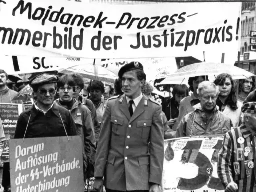 Demonstranten protestieren gegen das Majdanek-Urteil. Ein Mann in Uniform und ein Überlebender des Holocaust tragen Schilder, die gegen NS-Verbrechen und die Verjährung von Taten protestieren.
