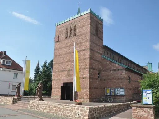 Kirche in Dettingen am Main mit roten Ziegeln, Fahnen und Statuen vor dem Eingang.