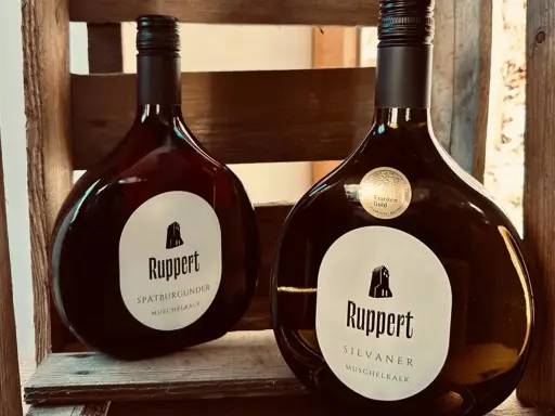 Zwei Flaschen Ruppert Wein, Spätburgunder und Silvaner, stehen in einer Holzkiste. Ein Zeichen für den Weinbau Franken.