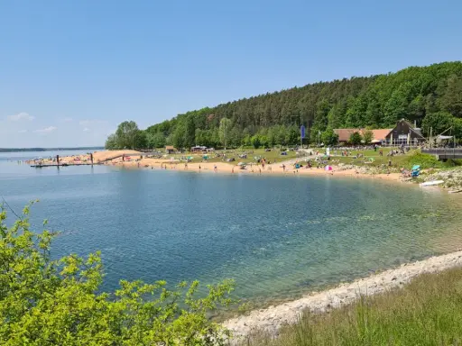 Sonniger Strandtag am Rothsee bei Heideck, Bayern. Menschen entspannen sich am Sandstrand, während Segelboote auf dem Wasser gleiten.