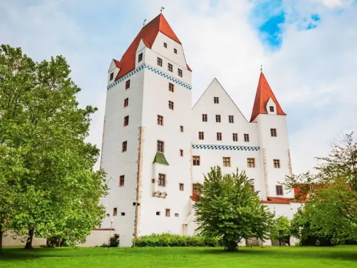 Das weiße Schloss Ingolstadt mit roten Dächern und grünen Bäumen im Vordergrund.