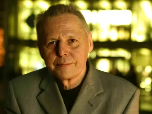 Porträt von Ulrich Enzensberger im Anzug, mit unscharfem, gelb beleuchtetem Hintergrund.