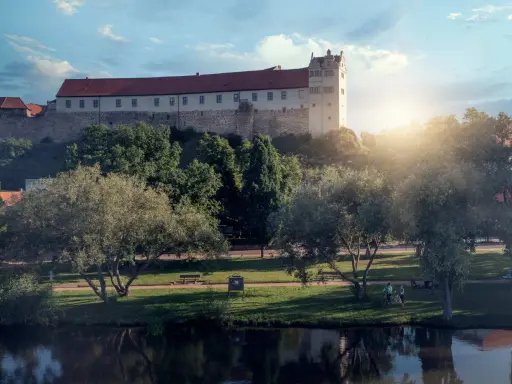 Schloss hinter Bäumen, ein Fluss im Vordergrund. Ein friedlicher Tag, wie ihn die Wettiner heute genießen könnten.