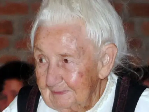 Porträt einer älteren Frau mit weißem Haar und traditioneller Kleidung. Traudl Well lächelt sanft.
