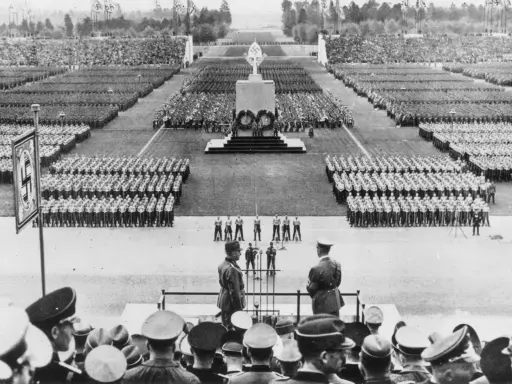 Massenveranstaltung in Nürnberg. Tausende marschieren, Fahnen wehen. Hitler ist anwesend.