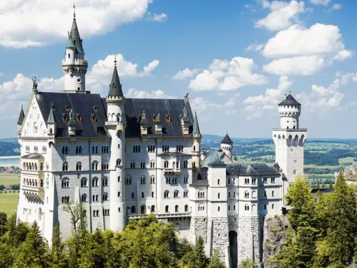 Schloss Neuschwanstein, ein Märchenschloss, dessen Geschichte von König Ludwig II. geprägt ist, thront majestätisch über grünen Hügeln und einem See.