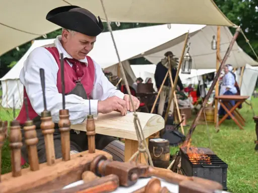 Ein Handwerker in historischer Kleidung arbeitet an Holz. Dies ist ein Beispiel dafür, was ist ein Freilichtmuseum: lebendige Geschichte zum Anfassen.