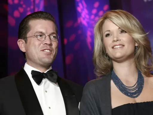Ein Mann mit Brille und Fliege, Karl-Theodor zu Guttenberg, und eine Frau mit blonden Haaren und blauer Kette.