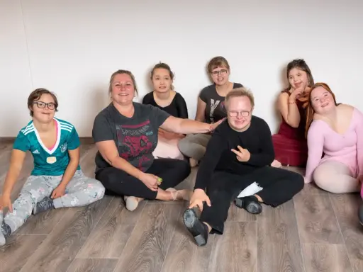 Gruppe von Menschen mit Down-Syndrom und einer Betreuerin sitzen auf dem Boden.