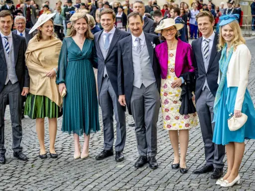 Gruppe von Personen in festlicher Kleidung, darunter Frauen in Kleidern und Männer in Anzügen.