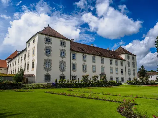 Schloss Waldburg-Zeil mit gepflegtem Garten und blauem Himmel mit Wolken.