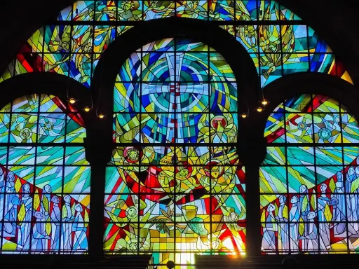 Farbenfrohe Glasmalerei eines Kirchenfensters mit biblischen Szenen und Engeln, die im Licht erstrahlen.