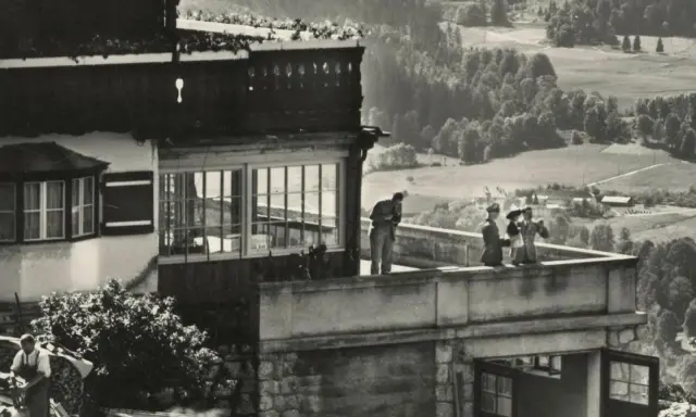 Blick auf die Hitler-Residenz mit Personen auf dem Balkon und einer malerischen Landschaft im Hintergrund.