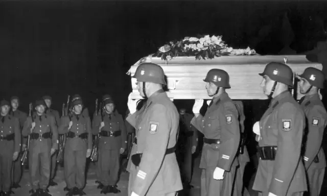 Militärische Ehreneskorte trägt einen mit Blumen geschmückten Sarg.