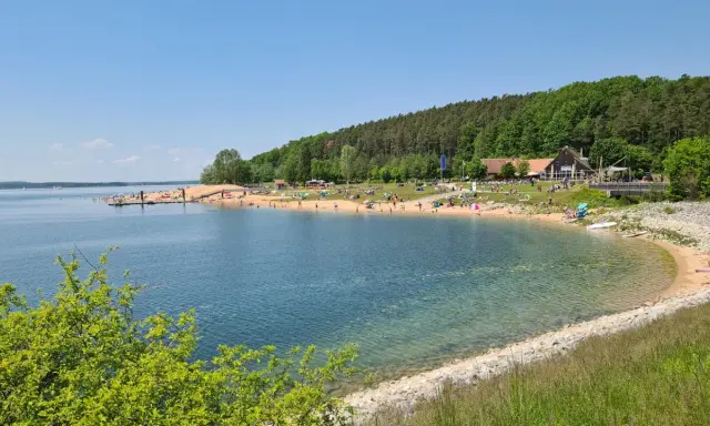 Sonniger Strandtag am Rothsee bei Heideck, Bayern. Menschen entspannen sich am Sandstrand, während Segelboote auf dem Wasser gleiten.