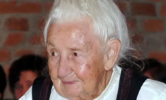 Porträt einer älteren Frau mit weißem Haar und traditioneller Kleidung. Traudl Well lächelt sanft.
