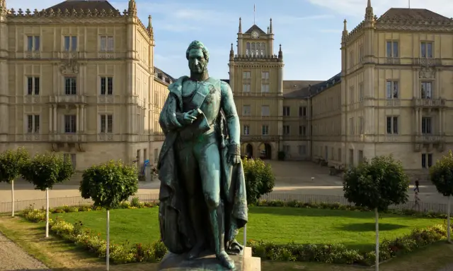 Bronzestatue von Ernst I. vor einem prächtigen Gebäude mit Turm und Arkaden.
