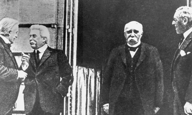 Vier Männer in Anzügen, die über den Friedensvertrag von Versailles diskutieren.