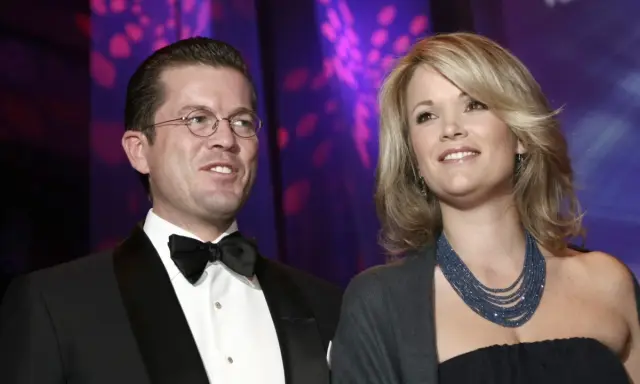 Ein Mann mit Brille und Fliege, Karl-Theodor zu Guttenberg, und eine Frau mit blonden Haaren und blauer Kette.