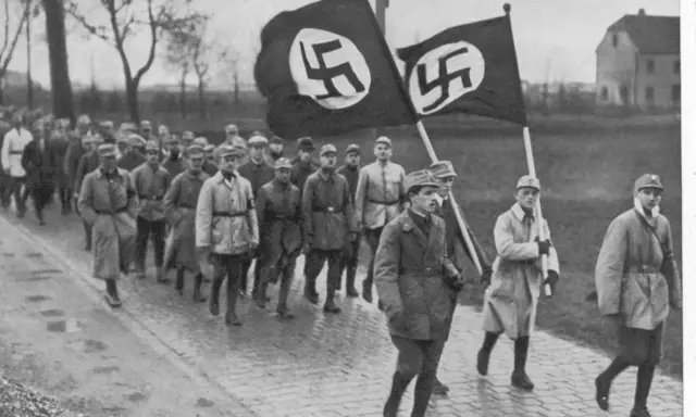 Männer marschieren mit Hakenkreuzfahnen. Ein historisches Bild, das an den Putschversuch Hitlers erinnert.