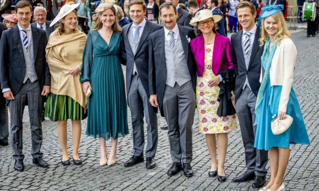 Gruppe von Personen in festlicher Kleidung, darunter Frauen in Kleidern und Männer in Anzügen.