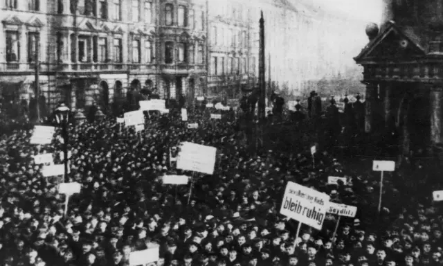 Massen demonstrieren in der Revolution 1918. Schilder mit Aufschriften wie "Seydlitz" und "Bleib ruhig" werden hochgehalten.
