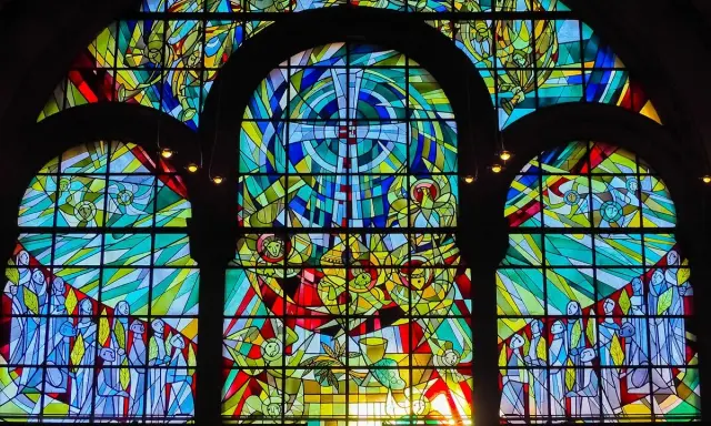 Farbenfrohe Glasmalerei eines Kirchenfensters mit biblischen Szenen und Engeln, die im Licht erstrahlen.
