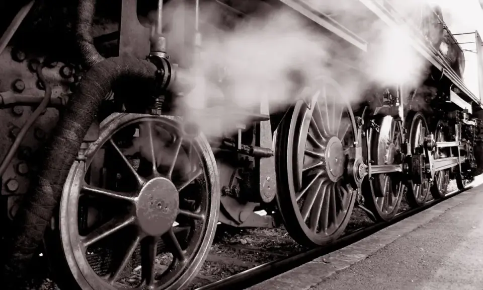 Dampf steigt auf von den Rädern einer historischen Lokomotive, ein Symbol für die Erfindung der Eisenbahn und den Beginn einer neuen Ära.