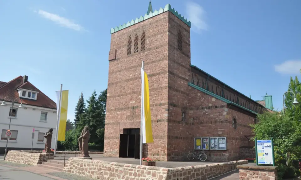 Kirche in Dettingen am Main mit roten Ziegeln, Fahnen und Statuen vor dem Eingang.