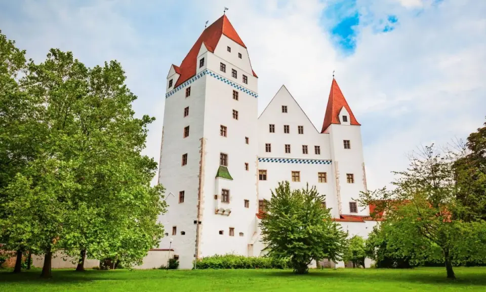 Das weiße Schloss Ingolstadt mit roten Dächern und grünen Bäumen im Vordergrund.