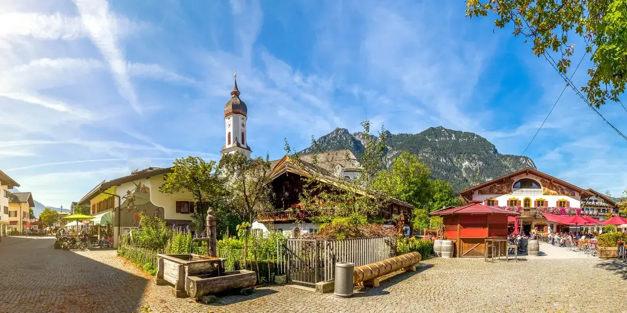 Idyllisches Dorf mit Kirche und Bergkulisse. Eine Szene, die an die Franken Geschichte erinnert, mit traditionellen H&auml;usern und einem belebten Platz.