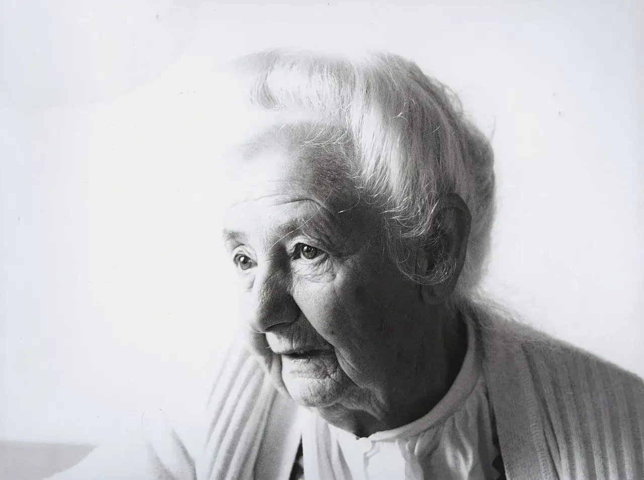 Porträt von Traudl Well, einer älteren Frau mit grauem Haar und Falten im Gesicht, die nachdenklich in die Ferne blickt.