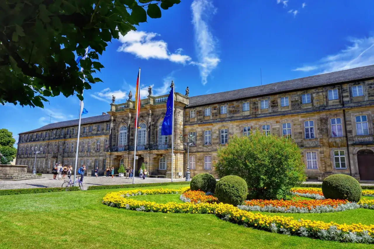 Markgrafen Bayreuth: Prachtvolles Neues Schloss mit bl&uuml;hendem Garten und Fahnen im Sonnenschein.