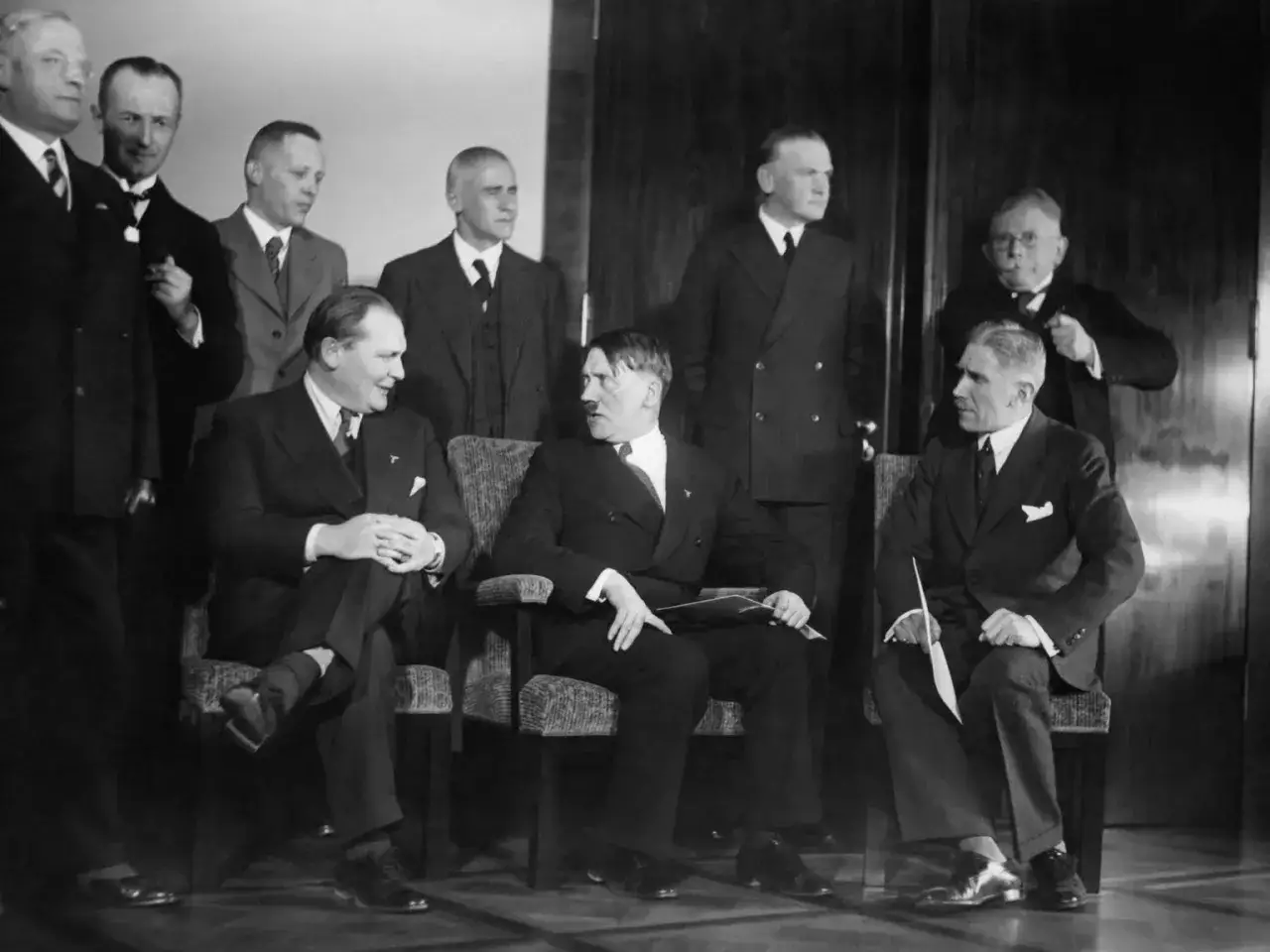 Am 30. Januar 1933: Hitler und seine Gefolgschaft, eine Gruppe von Männern in Anzügen, sitzen und stehen in einem Raum.