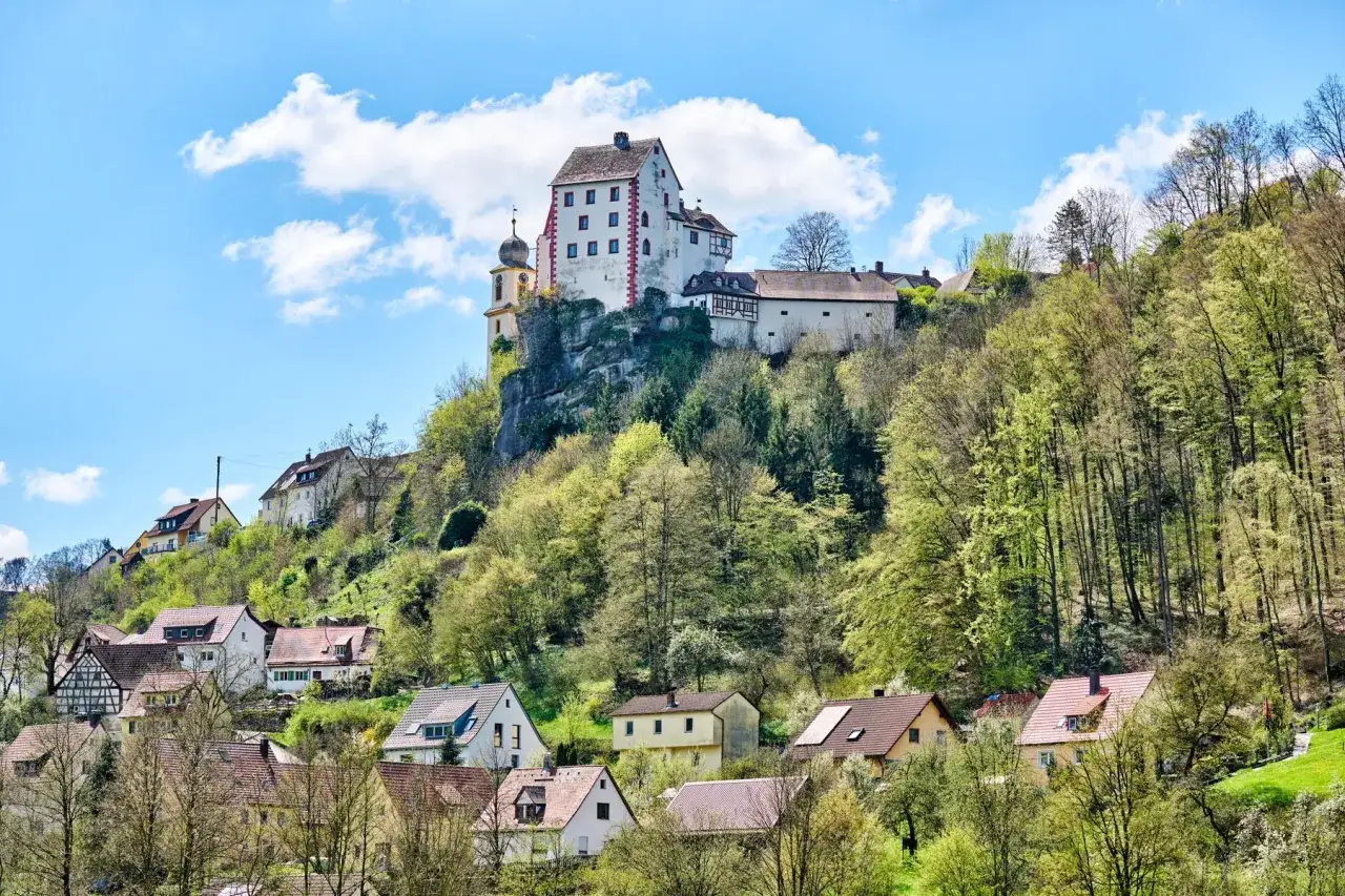 Burg und Dorf von Egloffstein thronen auf einem Felsen, umgeben von grünen Wäldern und blühendem Frühling.