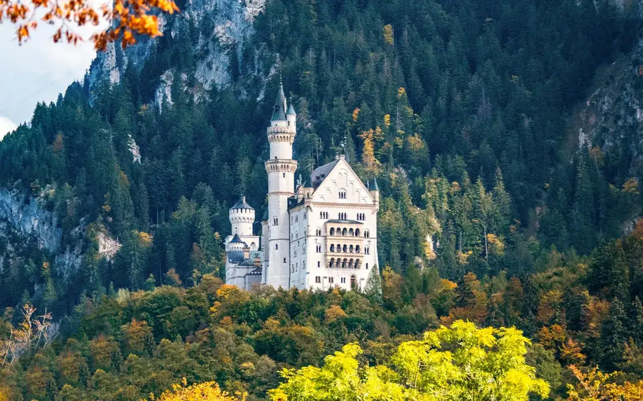 Schloss Neuschwanstein, ein Märchenschloss, thront auf einem Hügel vor einer Bergkulisse. Seine Geschichte ist eng mit König Ludwig II. verbunden.