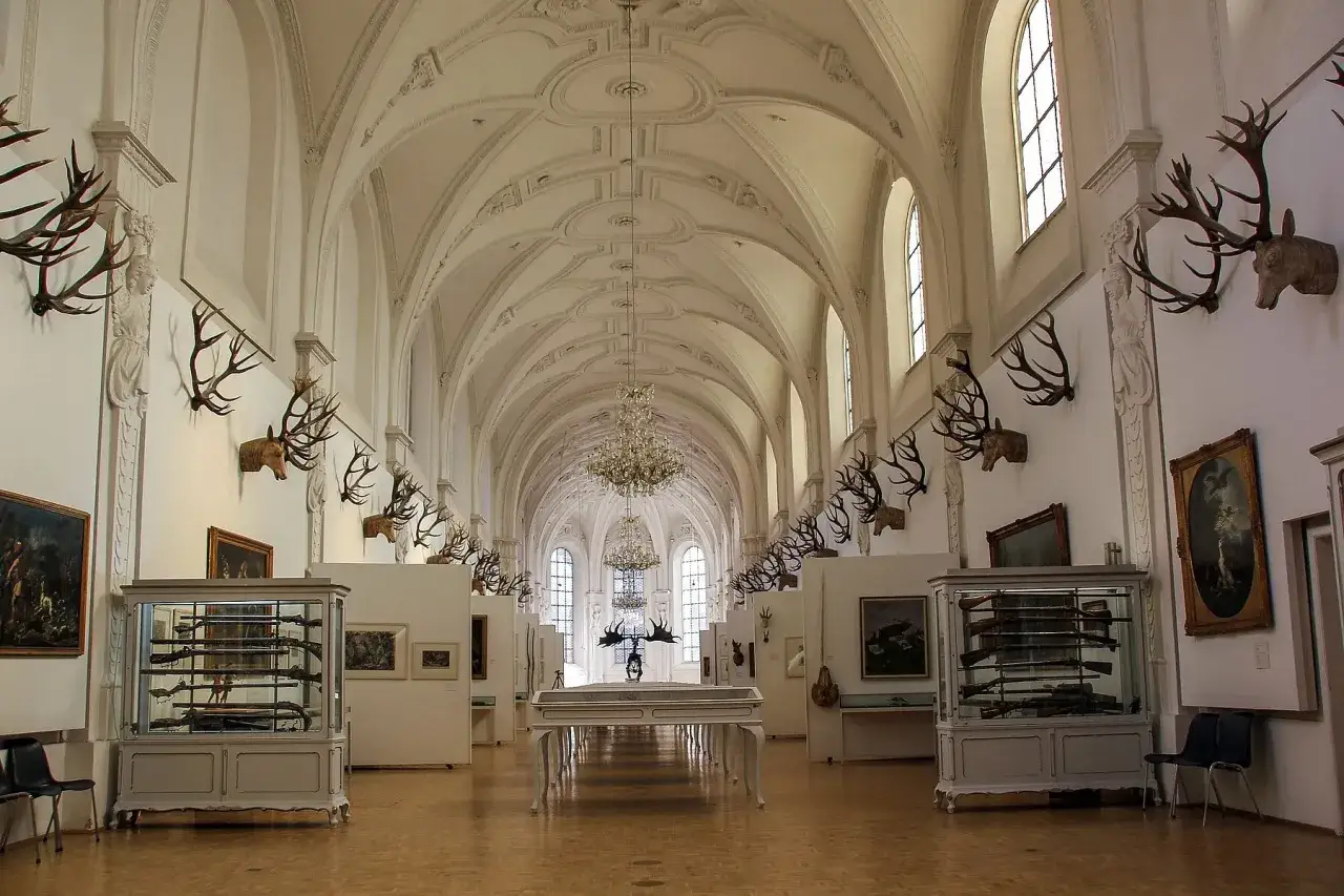 Prunkvolle Halle des deutschen Jagd- und Fischereimuseums mit Geweihen, Waffen in Vitrinen und Gem&auml;lden.