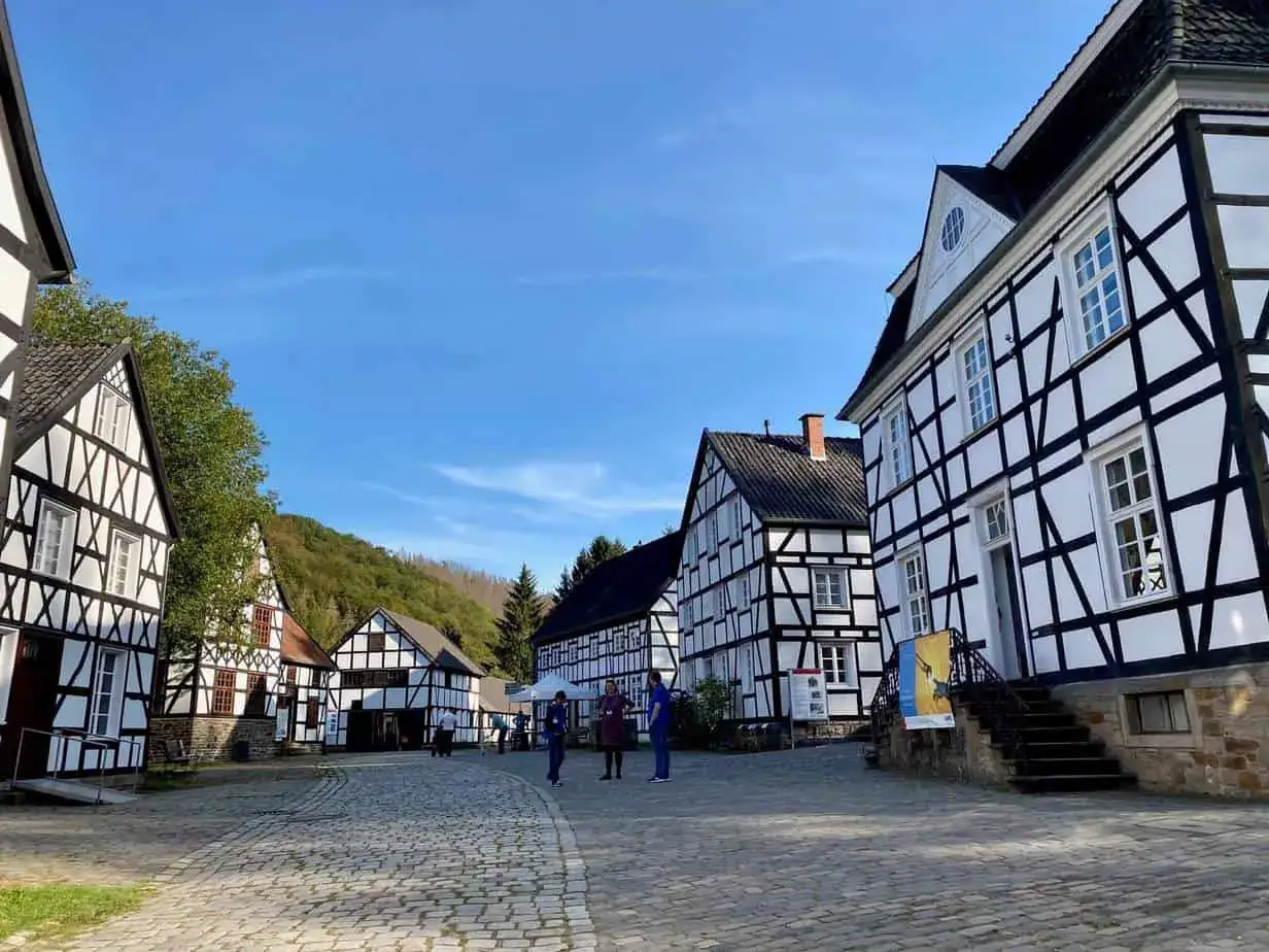 Fachwerkh&auml;user in einem Dorf, das zeigt, was ein Freilichtmuseum ist. Besucher schlendern &uuml;ber Kopfsteinpflaster unter blauem Himmel.