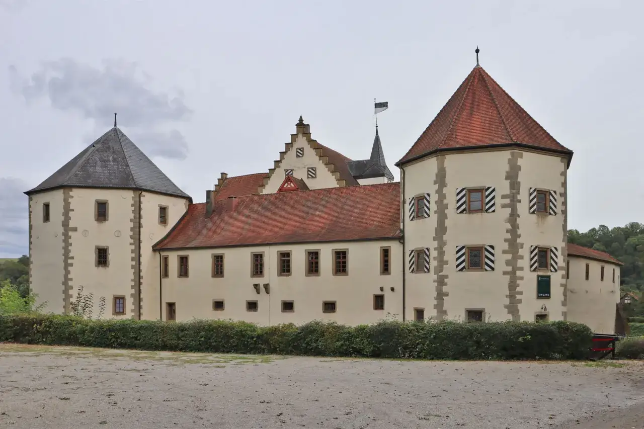 Eine Burg mit roten Ziegeldächern und einem runden Turm, der wie eine eiserne Faust in den Himmel ragt.